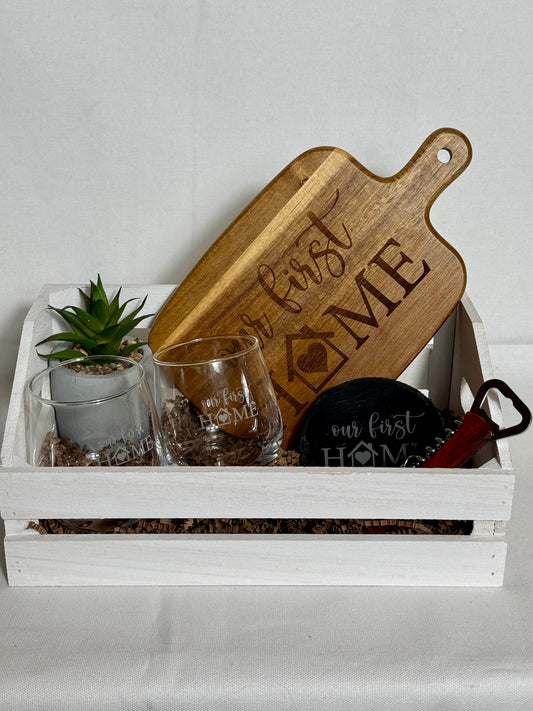Wooden cutting board with 'For First Home' engraving on a white tray with glasses and a plant.